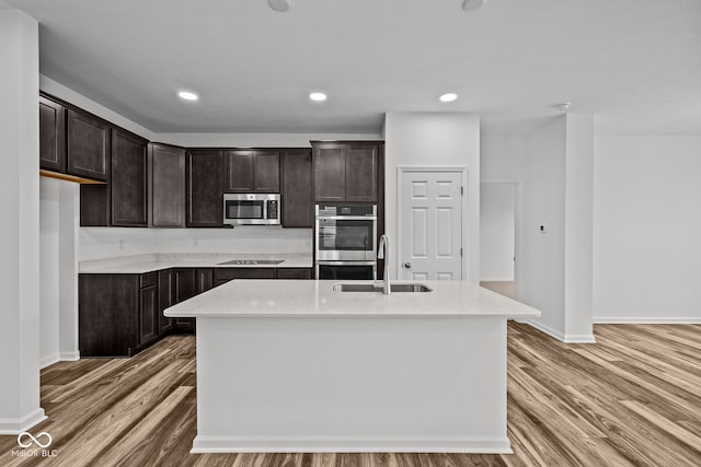 kitchen with dark brown cabinetry, sink, a kitchen island with sink, appliances with stainless steel finishes, and hardwood / wood-style floors