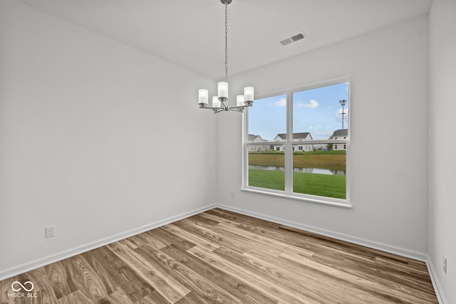 unfurnished dining area with a water view, a notable chandelier, and hardwood / wood-style flooring