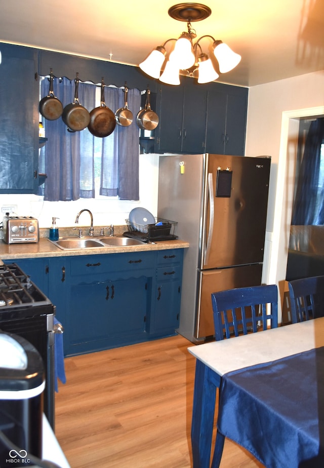 kitchen featuring an inviting chandelier, blue cabinetry, light wood-type flooring, stainless steel refrigerator, and sink