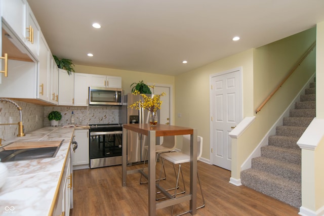 kitchen with backsplash, stainless steel appliances, sink, hardwood / wood-style flooring, and white cabinetry