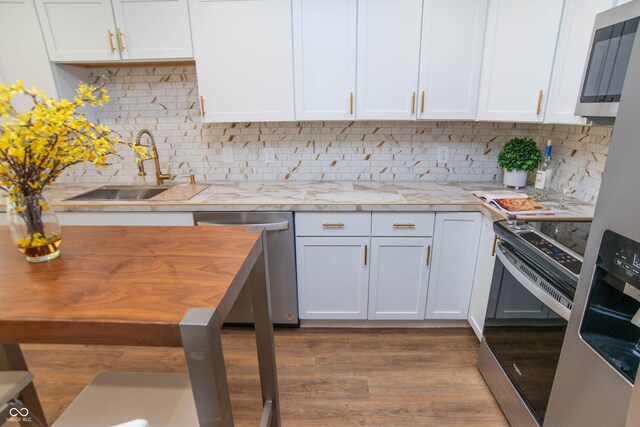 kitchen with appliances with stainless steel finishes, tasteful backsplash, sink, light hardwood / wood-style flooring, and white cabinets