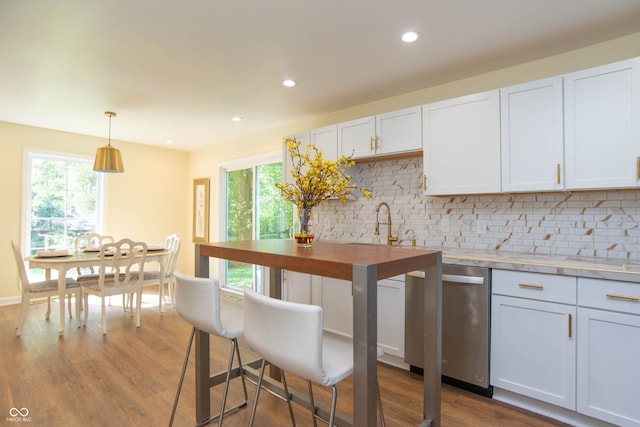 kitchen featuring stainless steel dishwasher, backsplash, pendant lighting, wood-type flooring, and white cabinets