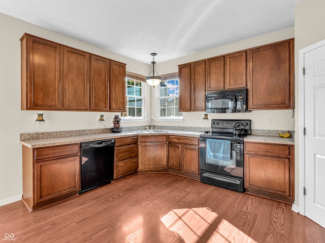 kitchen featuring decorative light fixtures, black appliances, sink, and light hardwood / wood-style flooring