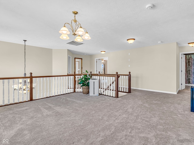 carpeted spare room with a textured ceiling and an inviting chandelier