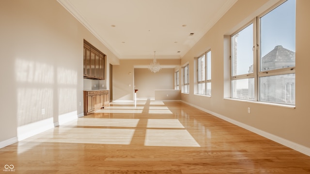 empty room with crown molding, light hardwood / wood-style flooring, and an inviting chandelier