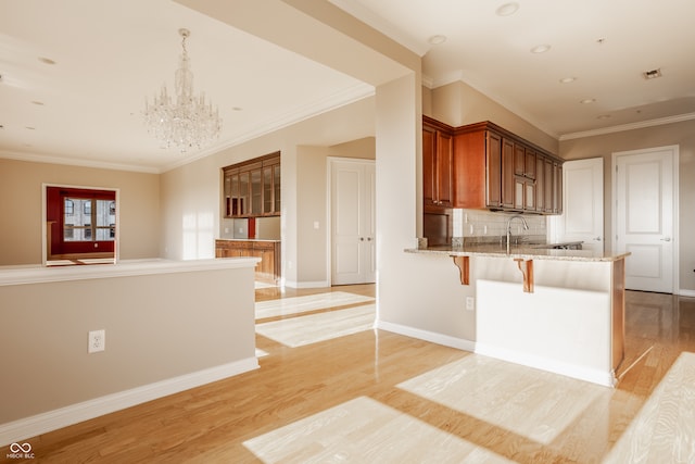 kitchen with crown molding, light hardwood / wood-style flooring, light stone counters, and kitchen peninsula