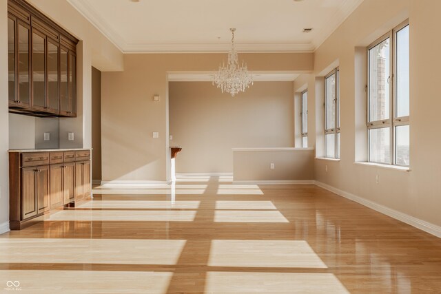 unfurnished dining area with plenty of natural light, ornamental molding, light hardwood / wood-style flooring, and a chandelier