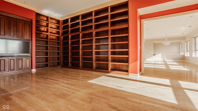 interior space with crown molding, a chandelier, light hardwood / wood-style flooring, and built in shelves