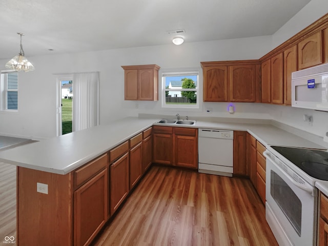 kitchen with an inviting chandelier, sink, wood-type flooring, kitchen peninsula, and white appliances