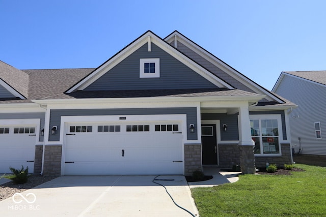 craftsman-style home with an attached garage, stone siding, a front yard, and driveway