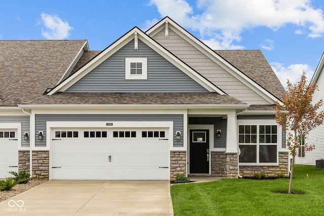 craftsman-style house featuring driveway, stone siding, roof with shingles, an attached garage, and a front yard