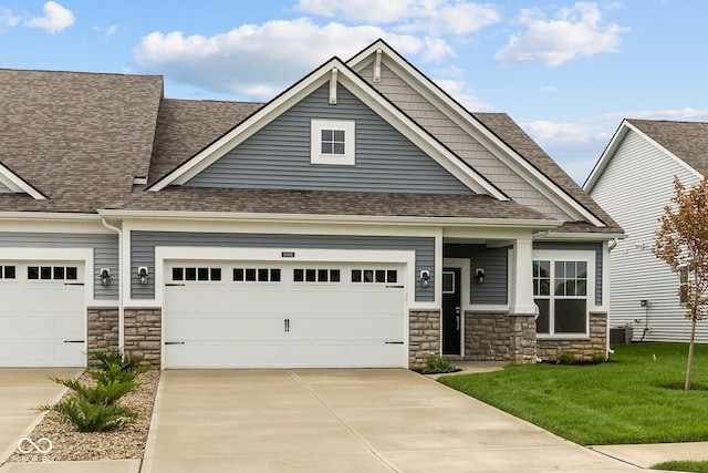 craftsman-style home featuring driveway, a garage, a shingled roof, stone siding, and a front yard