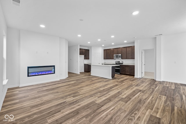 kitchen with appliances with stainless steel finishes, dark hardwood / wood-style floors, a center island with sink, and dark brown cabinets