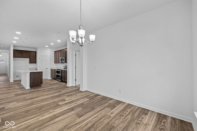 kitchen featuring a kitchen island, dark brown cabinetry, stainless steel appliances, hardwood / wood-style flooring, and decorative light fixtures