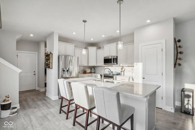 kitchen with backsplash, sink, appliances with stainless steel finishes, light hardwood / wood-style floors, and a kitchen island with sink