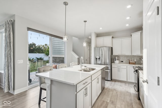 kitchen featuring appliances with stainless steel finishes, decorative light fixtures, light hardwood / wood-style floors, sink, and a kitchen island with sink