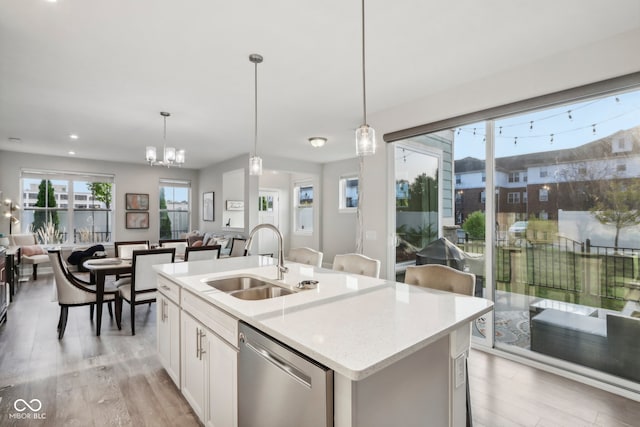 kitchen with hanging light fixtures, light hardwood / wood-style floors, dishwasher, sink, and a center island with sink