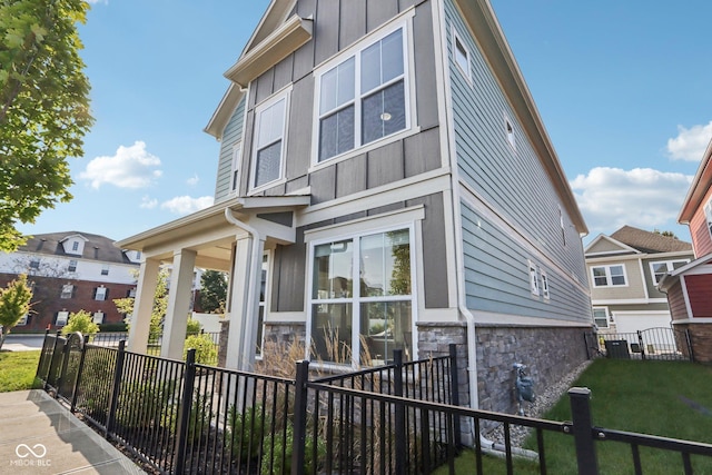 view of side of property featuring board and batten siding, stone siding, a yard, and a fenced front yard