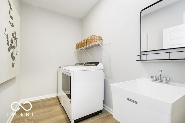 laundry area with light hardwood / wood-style floors, washing machine and clothes dryer, and sink