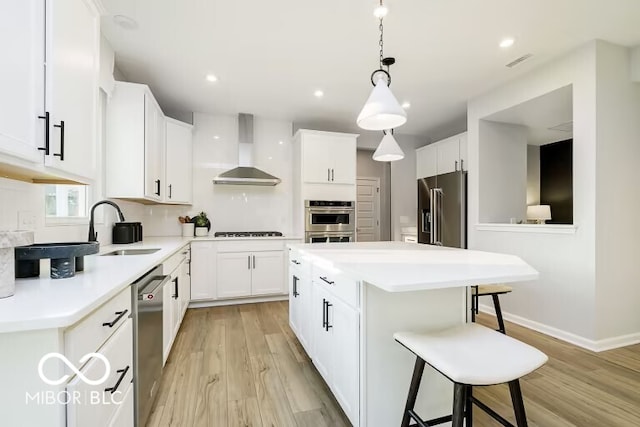 kitchen with light hardwood / wood-style floors, a kitchen island, stainless steel appliances, and wall chimney range hood