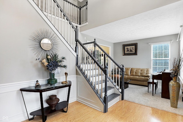 stairs with a wainscoted wall, a textured ceiling, and wood finished floors