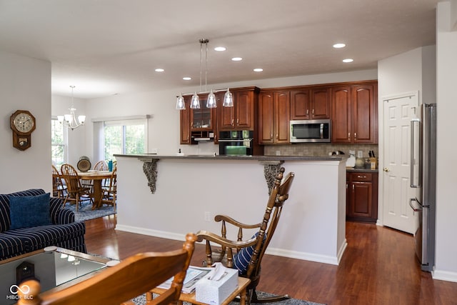 kitchen with dark hardwood / wood-style floors, decorative light fixtures, an inviting chandelier, appliances with stainless steel finishes, and a breakfast bar