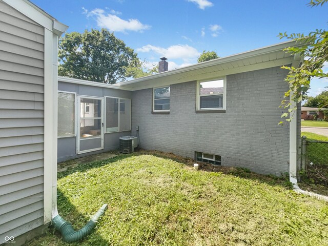 4013 N Graham Ave, Indianapolis, IN 46226 - view of home's exterior featuring a chimney, a lawn, central AC, brick siding, and a sunroom