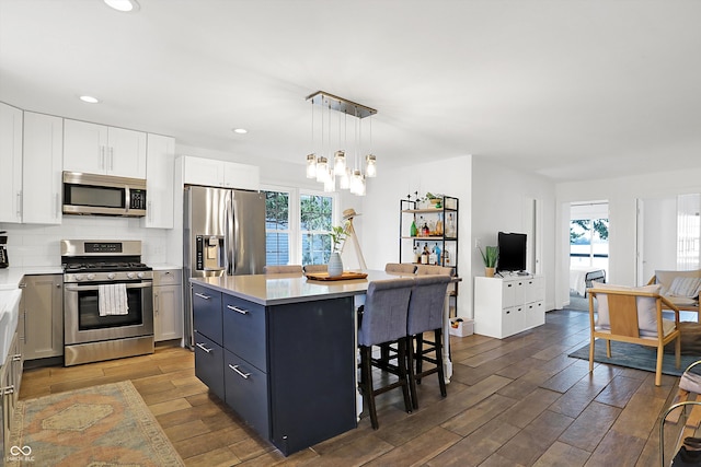 kitchen featuring pendant lighting, wood-type flooring, white cabinets, a center island, and stainless steel appliances