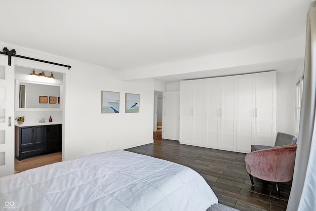 bedroom featuring sink, ensuite bathroom, wood-type flooring, and a barn door