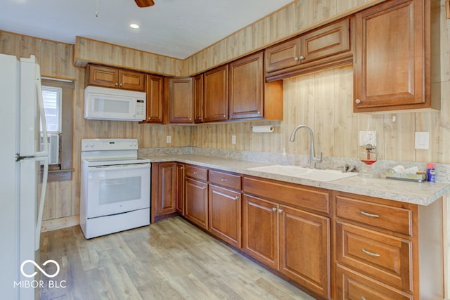 kitchen with light hardwood / wood-style floors, sink, wooden walls, white appliances, and ceiling fan