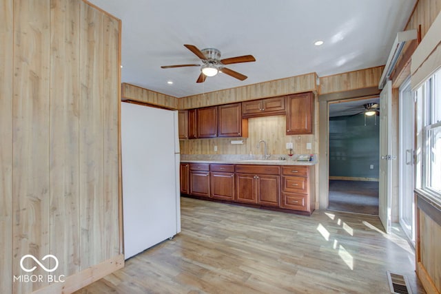 kitchen featuring light hardwood / wood-style floors, wood walls, white fridge, ceiling fan, and sink