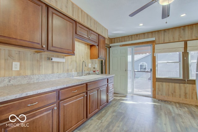 kitchen with ceiling fan, wooden walls, sink, and light hardwood / wood-style flooring