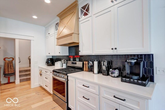 kitchen featuring stainless steel gas stove, tasteful backsplash, light countertops, light wood-style floors, and premium range hood