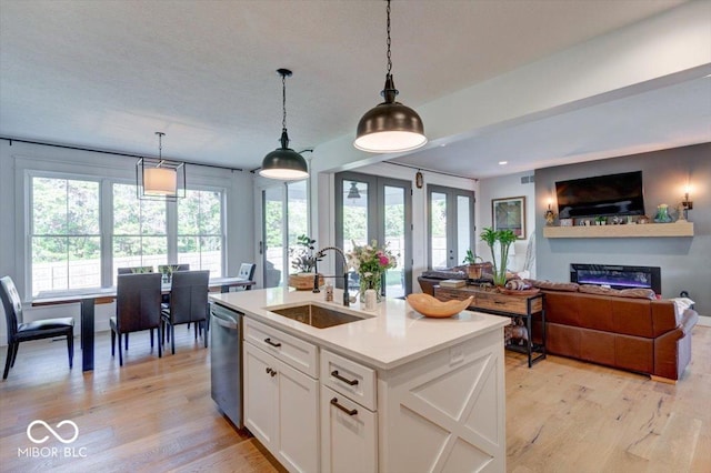 kitchen with light wood finished floors, white cabinets, a sink, light countertops, and stainless steel dishwasher