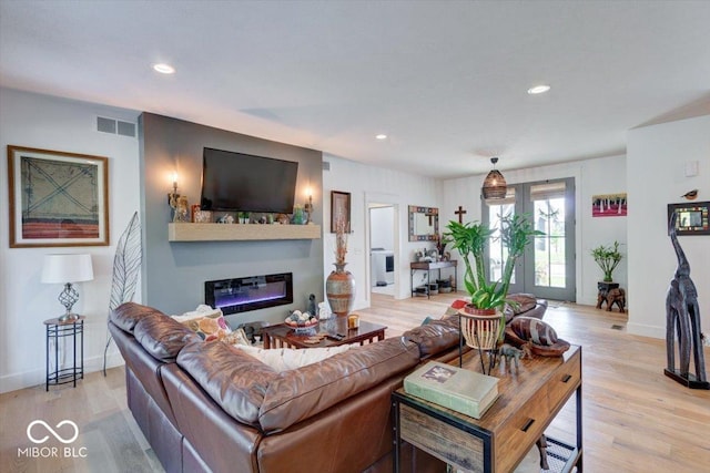 living room with visible vents, baseboards, a glass covered fireplace, light wood-style flooring, and recessed lighting