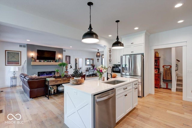 kitchen featuring light wood-style flooring, stainless steel appliances, a sink, visible vents, and open floor plan