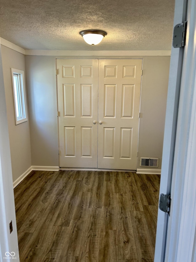 unfurnished bedroom featuring dark wood finished floors, a closet, visible vents, a textured ceiling, and baseboards