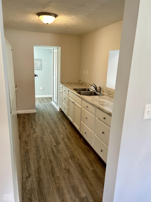 interior space with a textured ceiling, a sink, white cabinets, light countertops, and dark wood-style floors