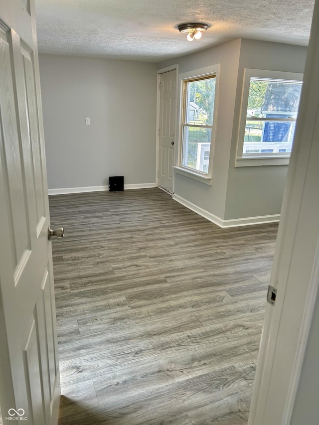 unfurnished room with a textured ceiling, wood finished floors, and baseboards