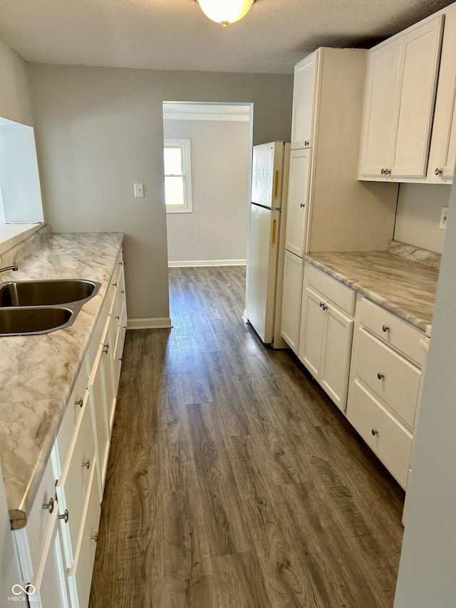 kitchen featuring dark wood-style floors, freestanding refrigerator, white cabinets, a sink, and baseboards