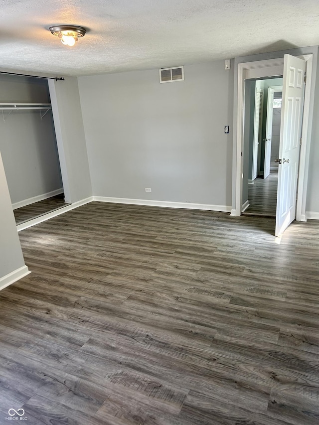 unfurnished bedroom with dark wood-style floors, a closet, visible vents, a textured ceiling, and baseboards