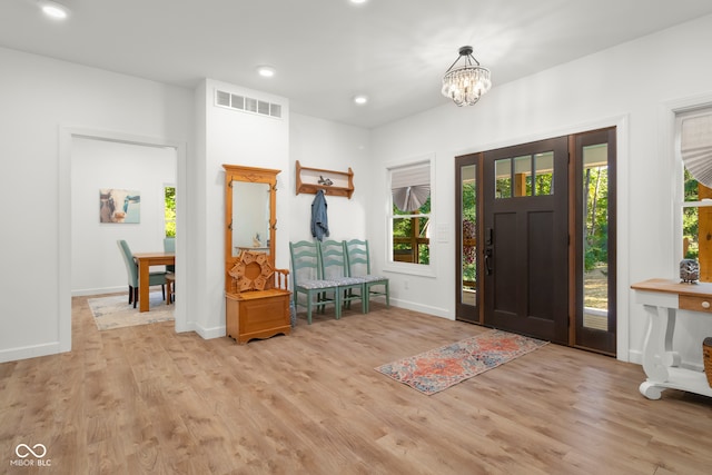 foyer entrance with a healthy amount of sunlight, a notable chandelier, and light wood-type flooring