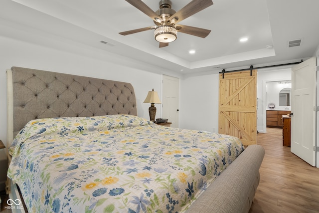 bedroom with a tray ceiling, light hardwood / wood-style flooring, ceiling fan, and a barn door