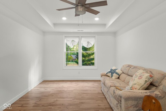 living room with a tray ceiling, light wood-type flooring, and ceiling fan