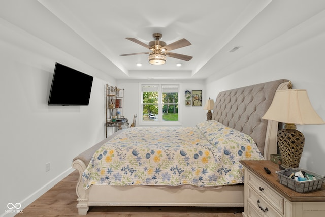 bedroom with a tray ceiling, wood-type flooring, and ceiling fan