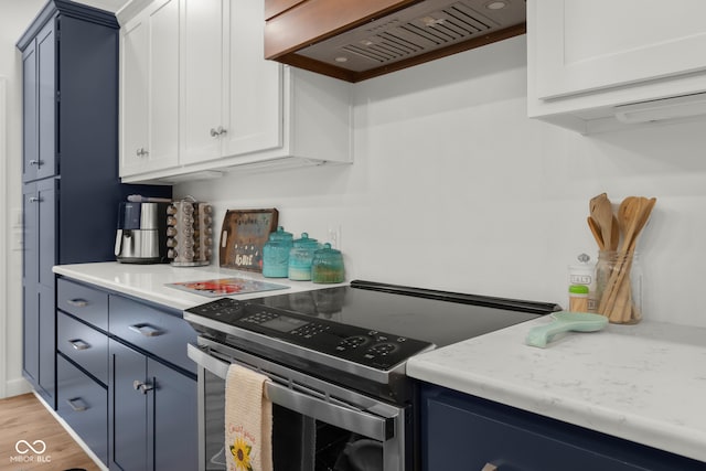 kitchen with custom exhaust hood, blue cabinetry, white cabinetry, light hardwood / wood-style flooring, and electric range