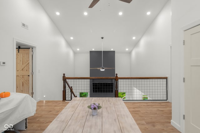 interior space featuring a barn door, ceiling fan, hardwood / wood-style flooring, and a towering ceiling