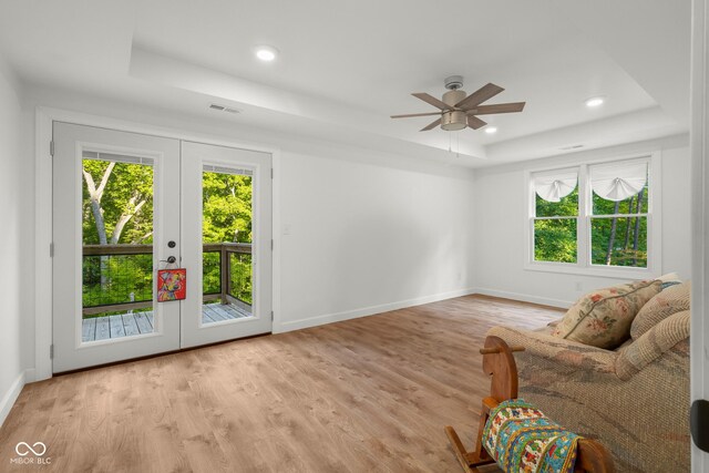 living room featuring a raised ceiling, a healthy amount of sunlight, light wood-type flooring, and ceiling fan