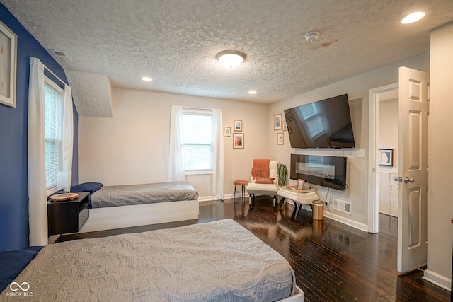 bedroom with dark wood-type flooring, a textured ceiling, and a multi sided fireplace