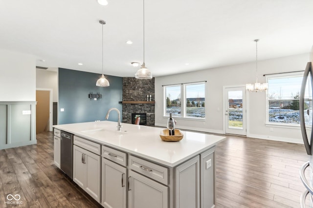 kitchen with a stone fireplace, an island with sink, pendant lighting, and sink